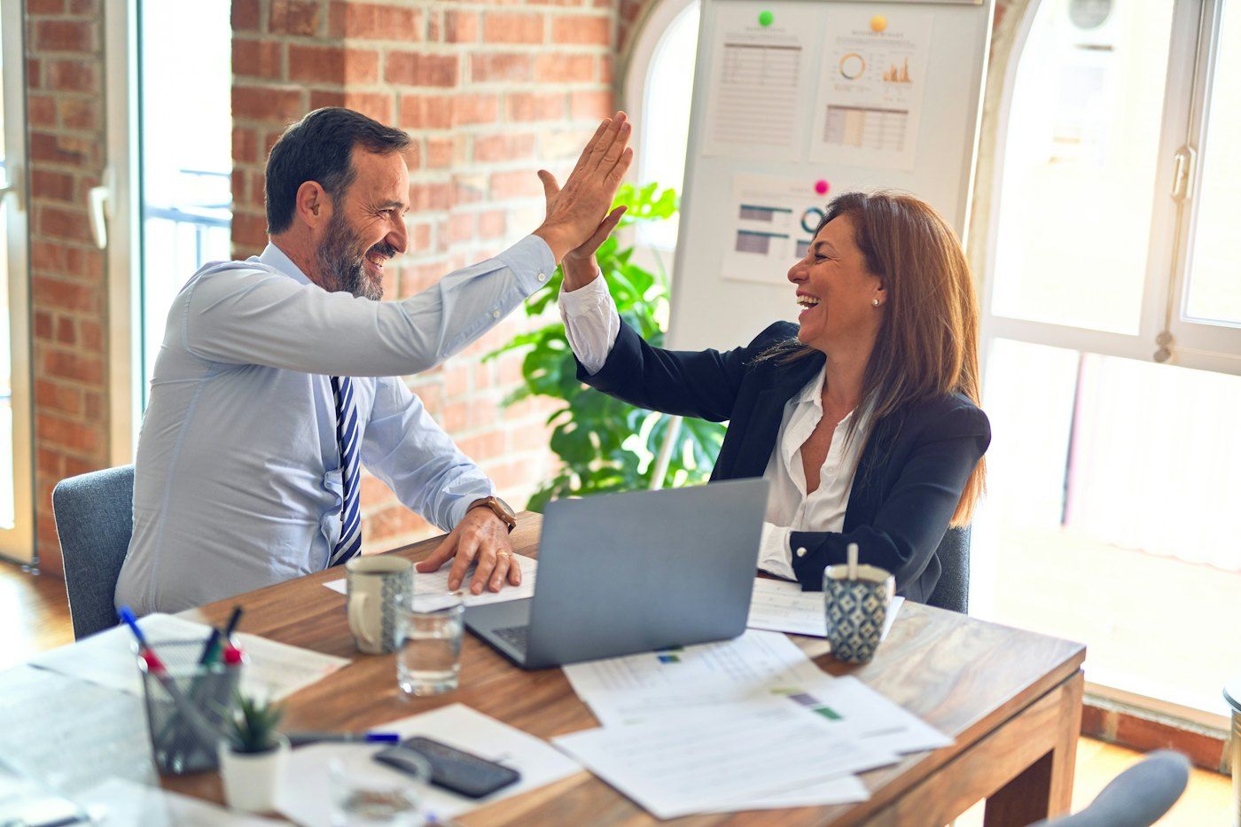 Two business partners sharing a high five at a bright office desk
